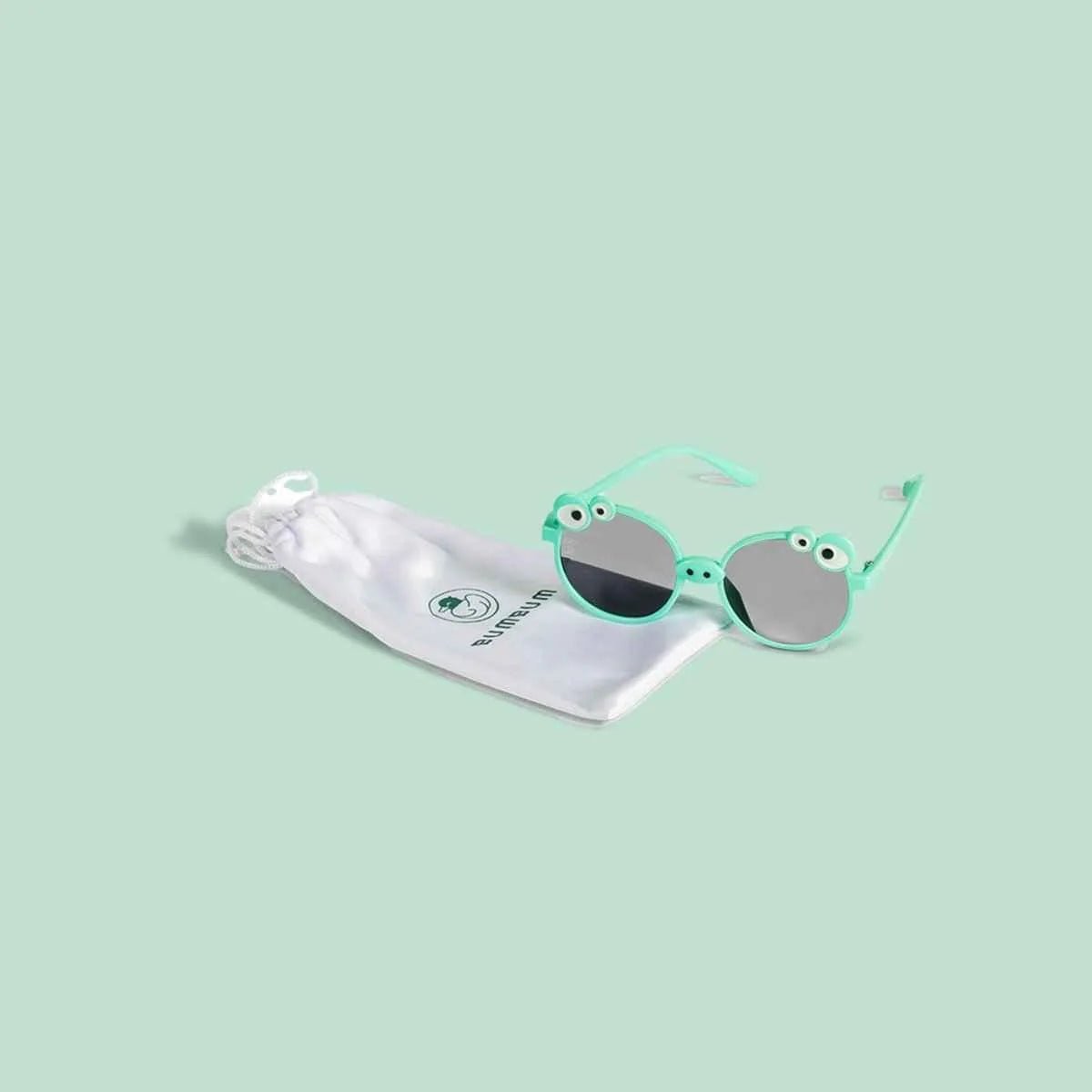 Children's sunglasses with green frames and reflective lenses on a light green background